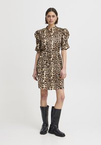 Leopardenmuster Kleid mit Puffärmeln, Druckknopfverschluss und tailliertem Schnitt. Kombiniert mit knielangen schwarzen Lederstiefeln mit Schnallendetails.