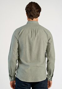 Zielona koszula z długim rękawem wykonana z teksturowanej tkaniny, z klasycznym kołnierzykiem i mankietami na guziki, z zaokrąglonym dołem i zakładką z tyłu.