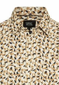 Kurze Herrenbluse mit Knopfleiste, beige mit einem geometrischen Muster in Braun und Schwarz. Aus Baumwolle gefertigt, mit klassischem Kragen und einer Tasche auf der Vorderseite.