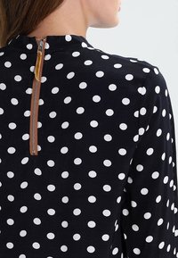 Top in tessuto nero con pois bianchi, con scollatura alta e chiusura zip con un accento marrone sul retro.