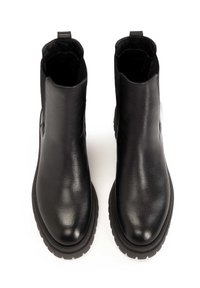 Para czarnych skórzanych botków za kostkę z zaokrąglonymi czubkami, grubymi gumowymi podeszwami i pętelkami z tyłu, widoczna z góry na białym tle.