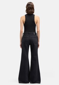 Zwart tanktop en zwarte flare jeans met een hoge taille, grote achterzakken en een gladden denimtextuur. Achteraanzicht compositie.