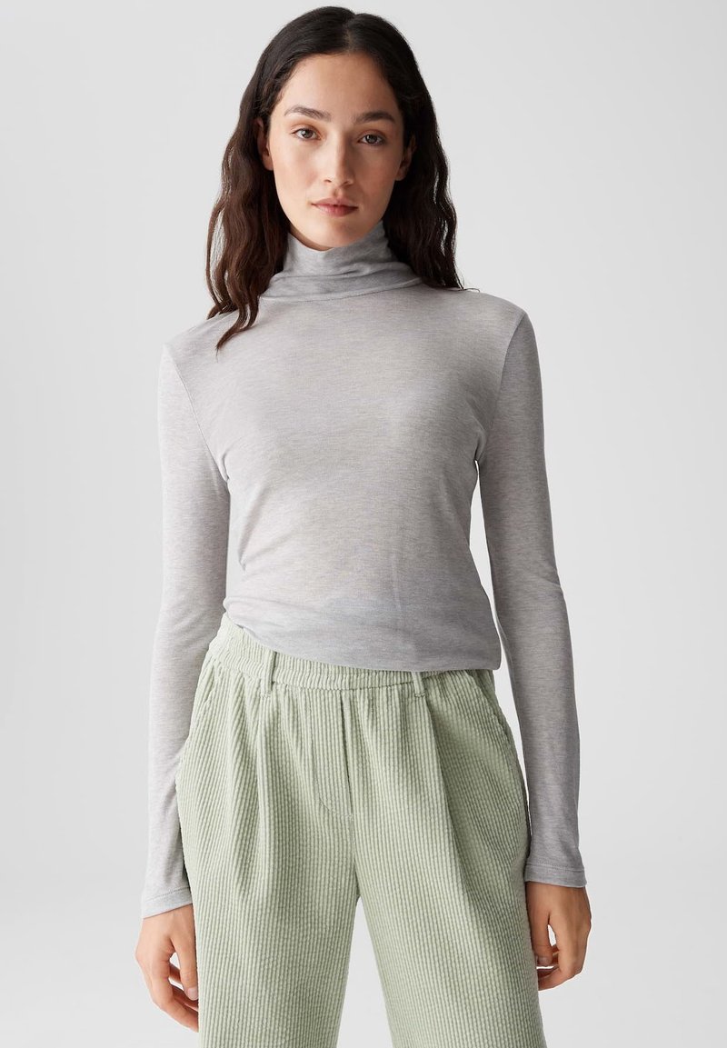 Grauer Langarmrollkragenpullover aus weichem Stoff, kombiniert mit hellgrünen, gerippten, strukturierten Hosen mit elastischem Bund.