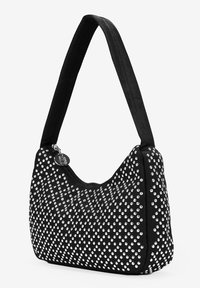 Bolso negro con forma curvada, adornado con tachuelas plateadas en un patrón de puntos, cuenta con una correa ancha y ajustable y cierre de cremallera.