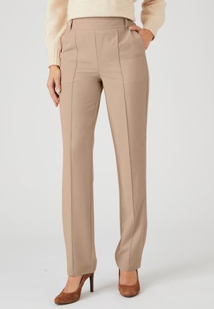 Pantaloni beige su misura realizzati in un tessuto liscio, con vita alta, cuciture laterali e gamba dritta; abbinati a tacchi marroni.