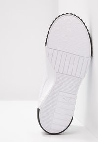 Zapatilla blanca con suela de goma texturizada, presenta una parte superior suave y acentos negros en la suela. Diseño simple y de perfil bajo.