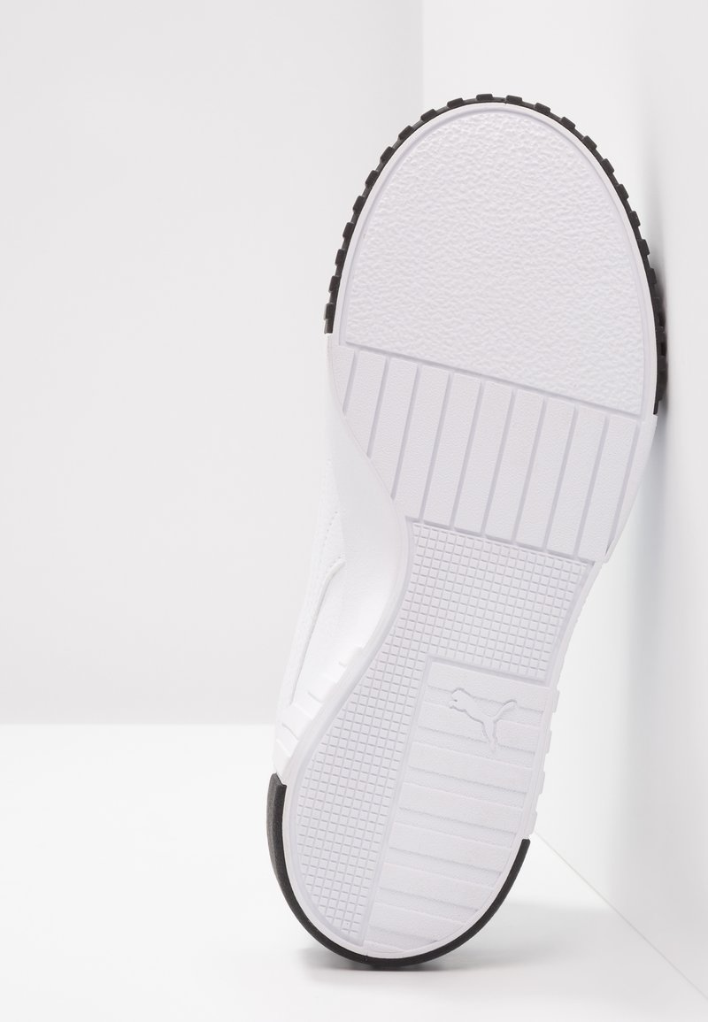 Baskets blanches avec une semelle en caoutchouc texturé, présentant un dessus lisse et des accents noirs sur la semelle extérieure. Design simple et profil bas.