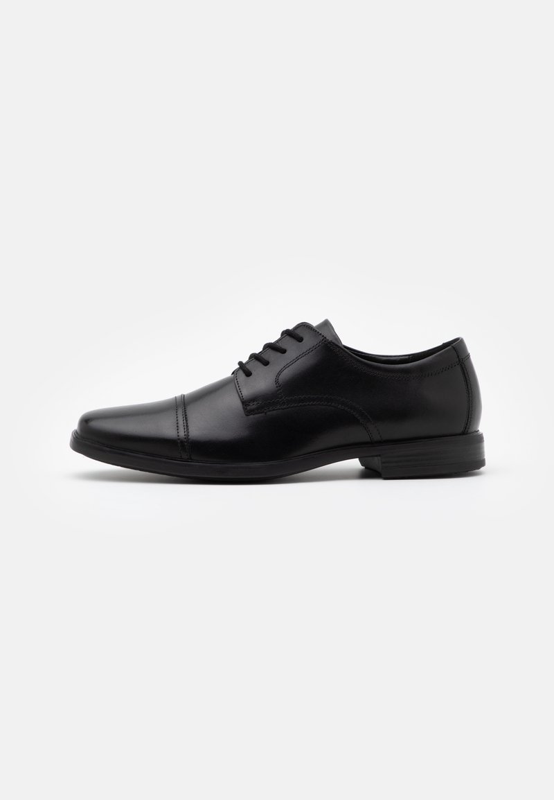 Chaussure de ville Oxford en cuir noir avec laçage fermé, couture sur bout droit et petit talon empilé sur fond blanc uni.