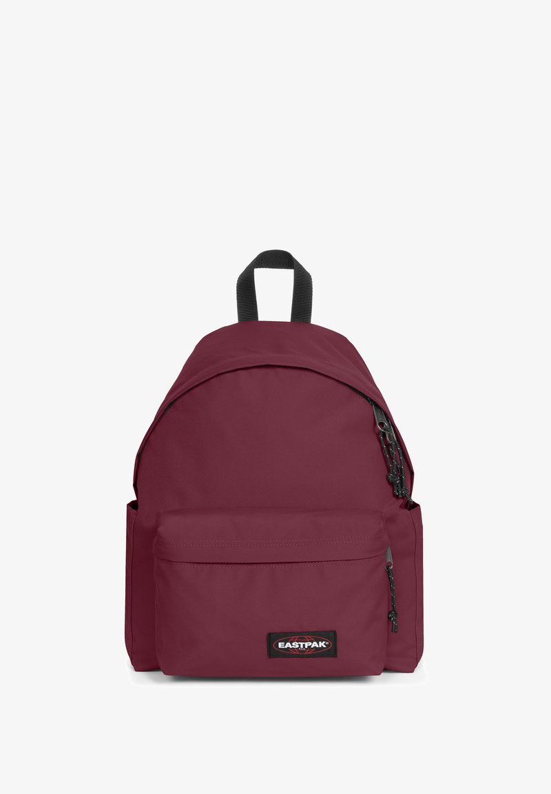 Červený látkový batoh s zakřiveným vrchem, nastavitelné popruhy, přední kapsa a logo nášivka. Obsahuje zipy a strukturovaný povrch.