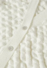 Cardigan en maille blanche texturée avec patte de boutonnage côtelée verticale et deux boutons ronds translucides visibles.