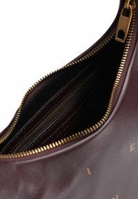 Borsa in pelle di un profondo bordeaux aperta, con una cerniera dorata e un compartimento interno con zip per una conservazione sicura.