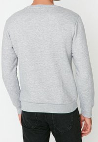 Sudadera gris con mangas largas, puños y dobladillo acanalados, textura de punto suave, diseño de cuello redondo y sin marcas ni patrones visibles.