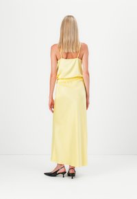 Gul sateng maxi-kjole med spagettistropper, elastisk midje og glatt tekstur. Svarte slingback-sko med spiss tå og lav hæl.