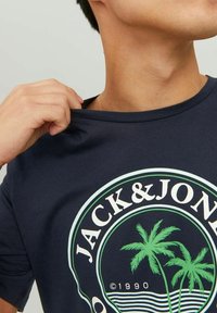 Marinblå kortärmad T-shirt i bomull med gröna palmträdsgrafik och texten "JACK & JONES" i en cirkulär design.
