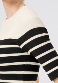 Maglia a righe nera e crema con maniche corte, caratterizzata da una texture a costine e un design a collo rotondo.