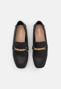 Černé loafers z umělé kůže se čtveratou špičkou, zdobené zlatým řetízkem a plochou podrážkou. Interior má béžovou podšívku s názvem značky.