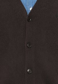 Brun stickad cardigan med V-hals, med fyra svarta knappar, texturerad tyg och en subtil logotyp nära halslinningen.