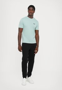 Mintgrønn kortermet T-skjorte med rund hals og en liten svart logo. Matchende med svarte smale joggebukser og hvite sneakers.