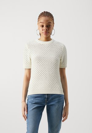 Knit short-sleeve sweater in off-white with textured open weave details, ribbed crew neckline and hem, paired with blue jeans.