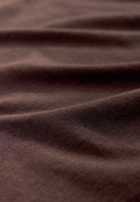 Material maro moale cu pliuri subtile și textură netedă, evidențiind detalii fine de tricotaj.