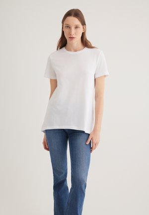 White cotton t-shirt with short sleeves, crew neck, relaxed fit, and a slightly longer back hem, paired with blue denim jeans.