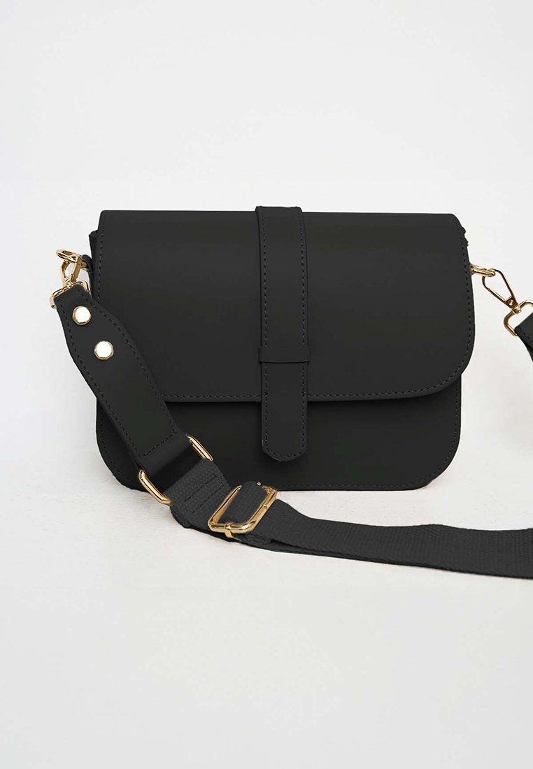 Zwarte faux leren crossbody tas met een omklapflap, gouden details en een afneembare stoffen schouderband. Voorzien van een knopsluiting en een plat ontwerp.