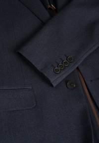 Navyblauer taillierter Blazer aus strukturiertem Stoff, mit Reverskragen, einer Brusttasche und fünf schwarzen Knöpfen am Ärmel.