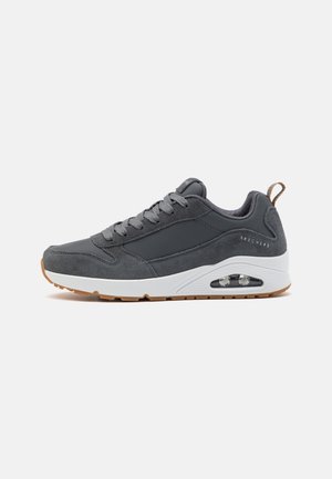 Baskets Skechers grises avec dessus en daim et cuir, semelle blanche avec coussin d'air visible, et languette marron au talon.