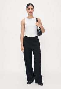 White sleeveless top paired with high-waisted black wide-leg trousers. Accessories include a small black textured handbag and hoop earrings.