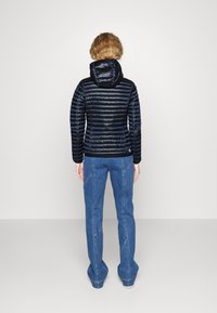 Giacca puffer blu navy con cuciture orizzontali e cappuccio, abbinata a jeans in denim blu chiaro a zampa d'elefante con dettagli sulle cuciture.