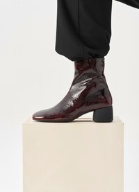 Burgundowe lakierowane botki za kostkę z ostro wciętym czubkiem i masywnym czarnym obcasem, charakteryzujące się gładką, błyszczącą powierzchnią i dopasowanym krojem.