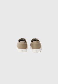 Baskets en toile beige au design bas, semelles en caoutchouc blanches et branding discret sur le talon. Texture lisse avec un minimum de détails.