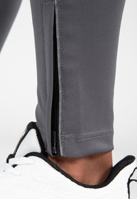 Grijze sportlegging met een rits bij de enkel, gemaakt van gladde, rekbare stof. Een witte sportschoen is gedeeltelijk zichtbaar aan de onderkant.