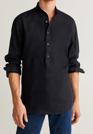 Mann trägt ein schwarzes Leinenhemd mit langen Ärmeln, Stehkragen und Drei-Knopf-Leiste, Ärmel hochgekrempelt, kombiniert mit blauen Jeans.