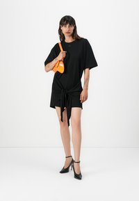 Black oversized t-shirt dress with a knotted front detail. Features short sleeves and a smooth texture. Accented with a small logo.