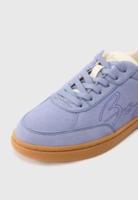 Vijolični semiš športni copat z gumijastim podplatom v barvi gume, z našitimi detajli in luknjicami na sprednjem delu. Čipke so svetlo modre.