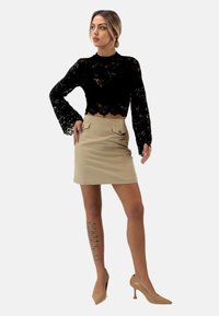 Sort blonde langærmet crop top med flagrende ærmer, parret med en beige knælang nederdel med to knapdetaljer. Nude stiletter.