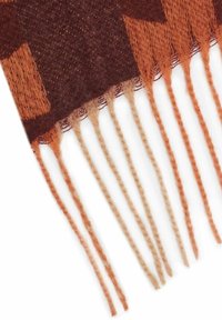Close-up of a brown and orange woven scarf edge with long twisted fringe tassels on a white background.