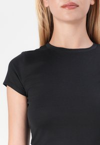 Juodas trumpomis rankovėmis marškinėliai, pagaminti iš minkštos medžiagos, su apvaliu iškirpimu ir prigludusia forma. Lygus audinys su minimaliais dizaino akcentais.