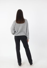Grijze gebreide trui met een losse pasvorm en verlaagde schouders, gecombineerd met zwarte rechte jeans. Eenvoudige textuur, geen zichtbare patronen of accenten.