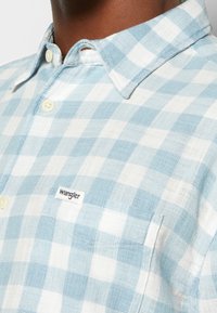 Ljusblå och vit rutmönstrad kortärmad skjorta med button-down-krage, med en liten "Wrangler"-etikett på fickan.