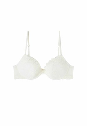 Soutien-gorge en dentelle blanche avec des coussins, des bords en forme de vagues, un motif floral délicat, des bretelles ajustables et une fermeture à crochets dans le dos.