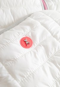 Witte gewatteerde stof met een klein rood rond patch met een zilveren honden silhouet embleem in het midden.