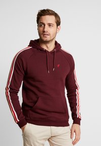 Maroon hoodie with drawstring, front pocket, and white-red stripes on sleeves. Soft fabric, ribbed cuffs and hem, logo on chest.