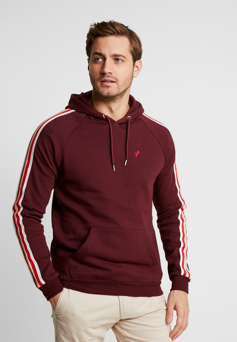 Maroon hoodie with drawstring, front pocket, and white-red stripes on sleeves. Soft fabric, ribbed cuffs and hem, logo on chest.