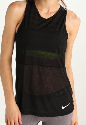 Frau trägt ein ärmelloses schwarzes Nike Tanktop und graue Leggings, mit dem Nike-Logo sichtbar nahe dem Saum auf der rechten Seite.