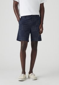 Bermude bleumarin cu un model texturat de puncte mici, având buzunare laterale și o croială lejeră, asortate cu adidași albi și un tricou.