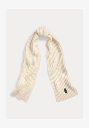 Cremefarbener, gerippter Strickschal mit einem kleinen bestickten Bären, der an einem Ende eine blaue Jacke trägt.