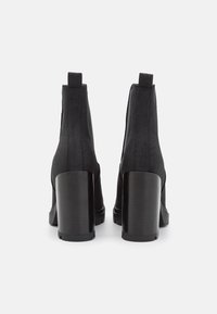 Botines negros con parte superior de tela lisa, paneles laterales elásticos y tacones gruesos negros. Presenta una puntera redondeada y un diseño minimalista.