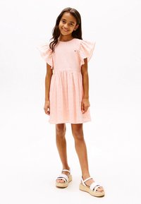 Ružové šaty z ľahkej látky s volánovými rukávmi, priliehavým živôtikom a rozšírenou sukňou. Kombinované s bielymi platformovými sandálmi.